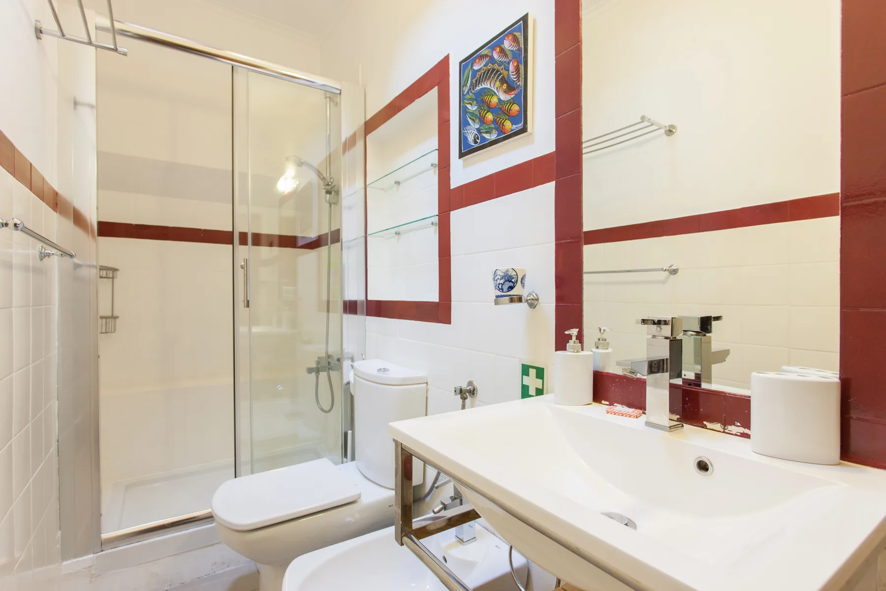 A bright tiled bathroom with a glass shower and a wide sink counter.