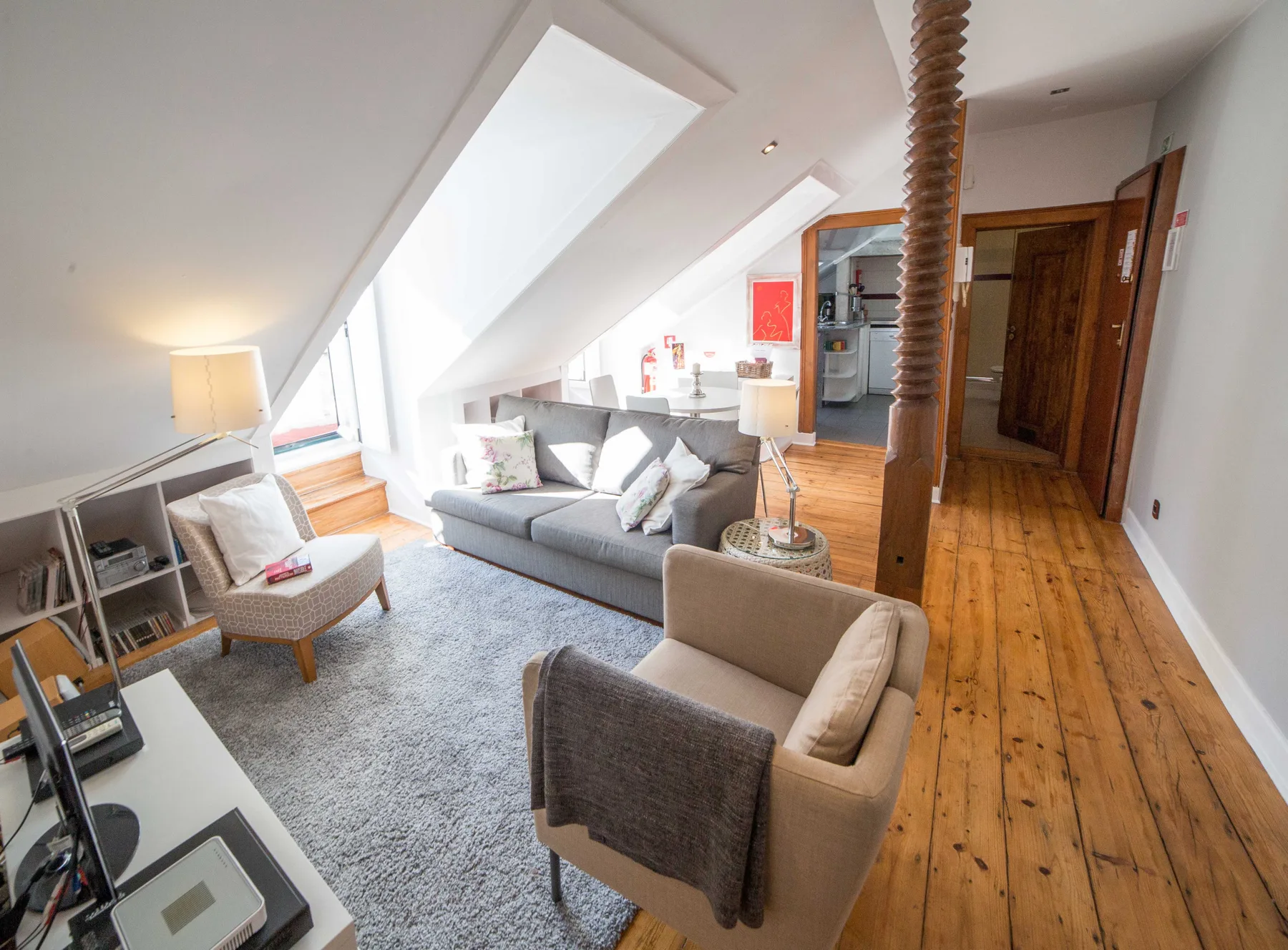 A bright attic living room has seating arranged around a gray rug beneath sloped ceilings.