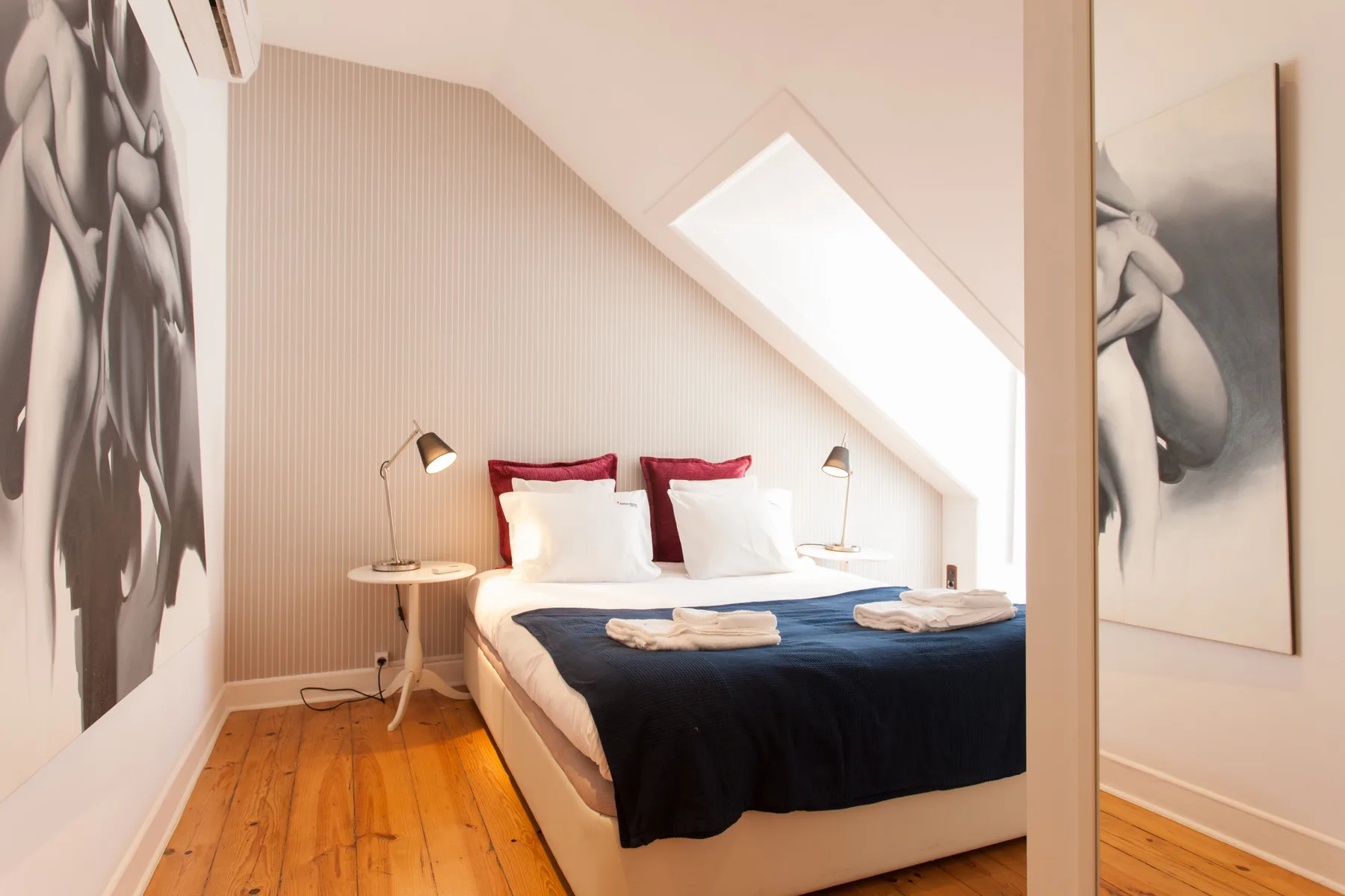 A bedroom with a bed beneath a sloped ceiling and framed wall art.
