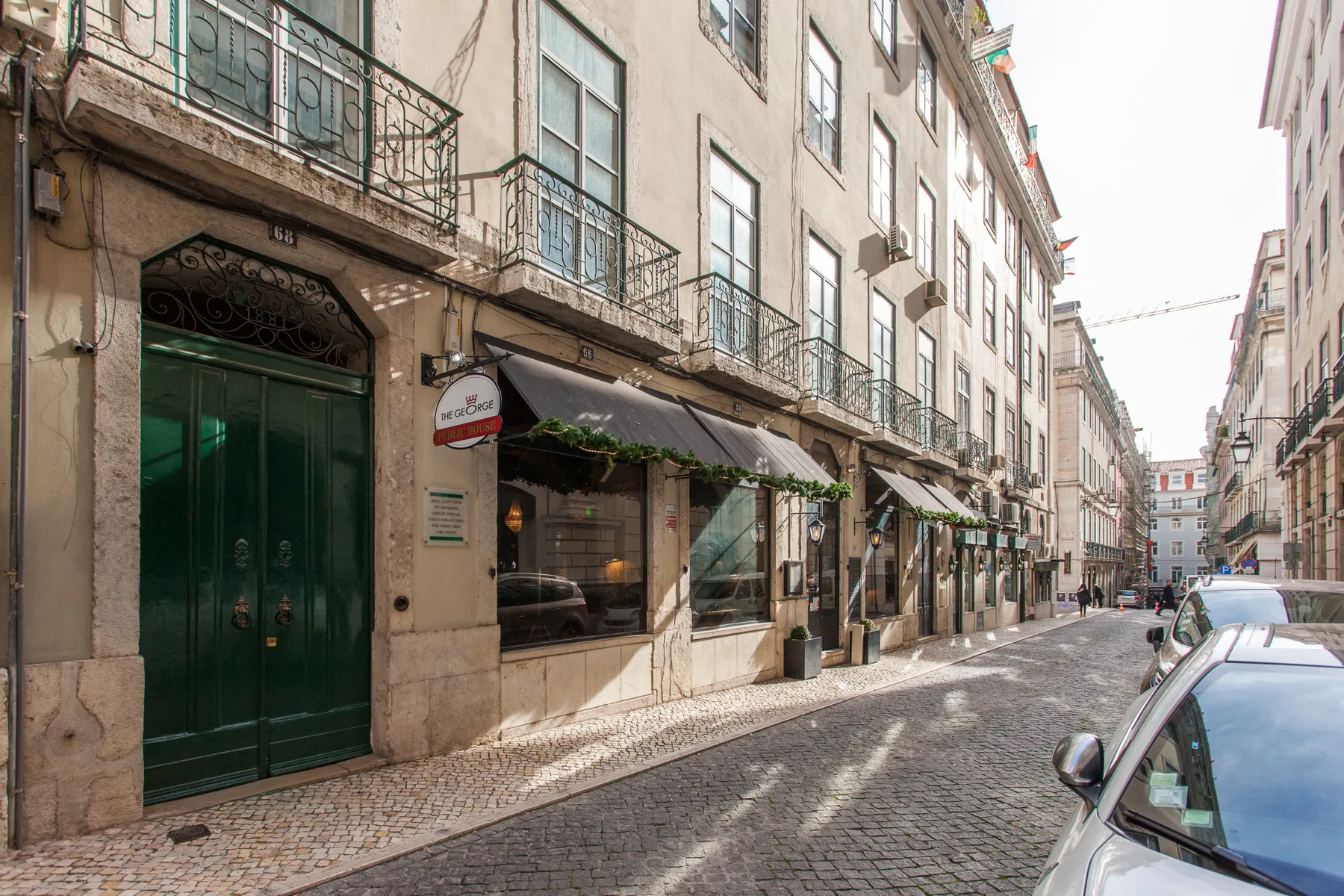 A narrow cobblestone street lined with multi-story buildings and storefronts.