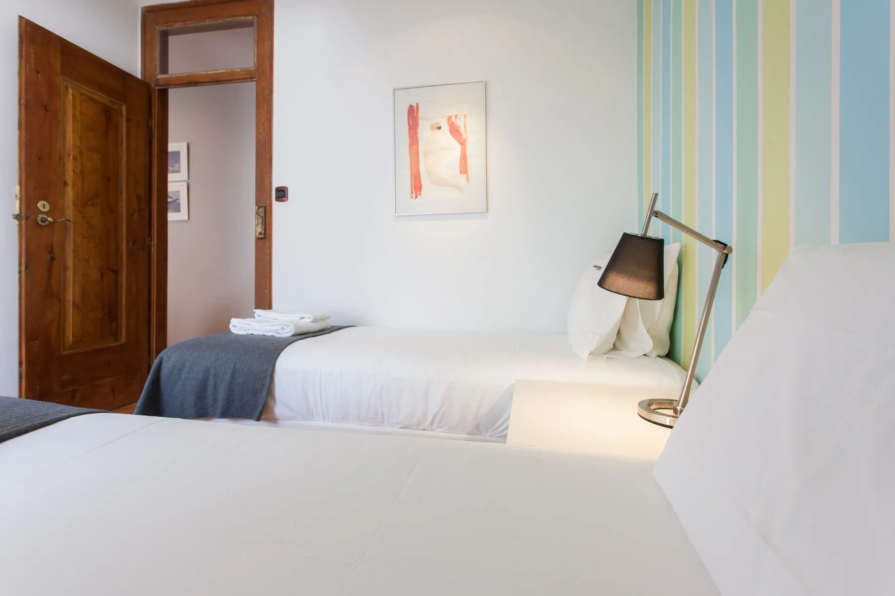 A bedroom with white beds, a bedside lamp, and a wooden door.