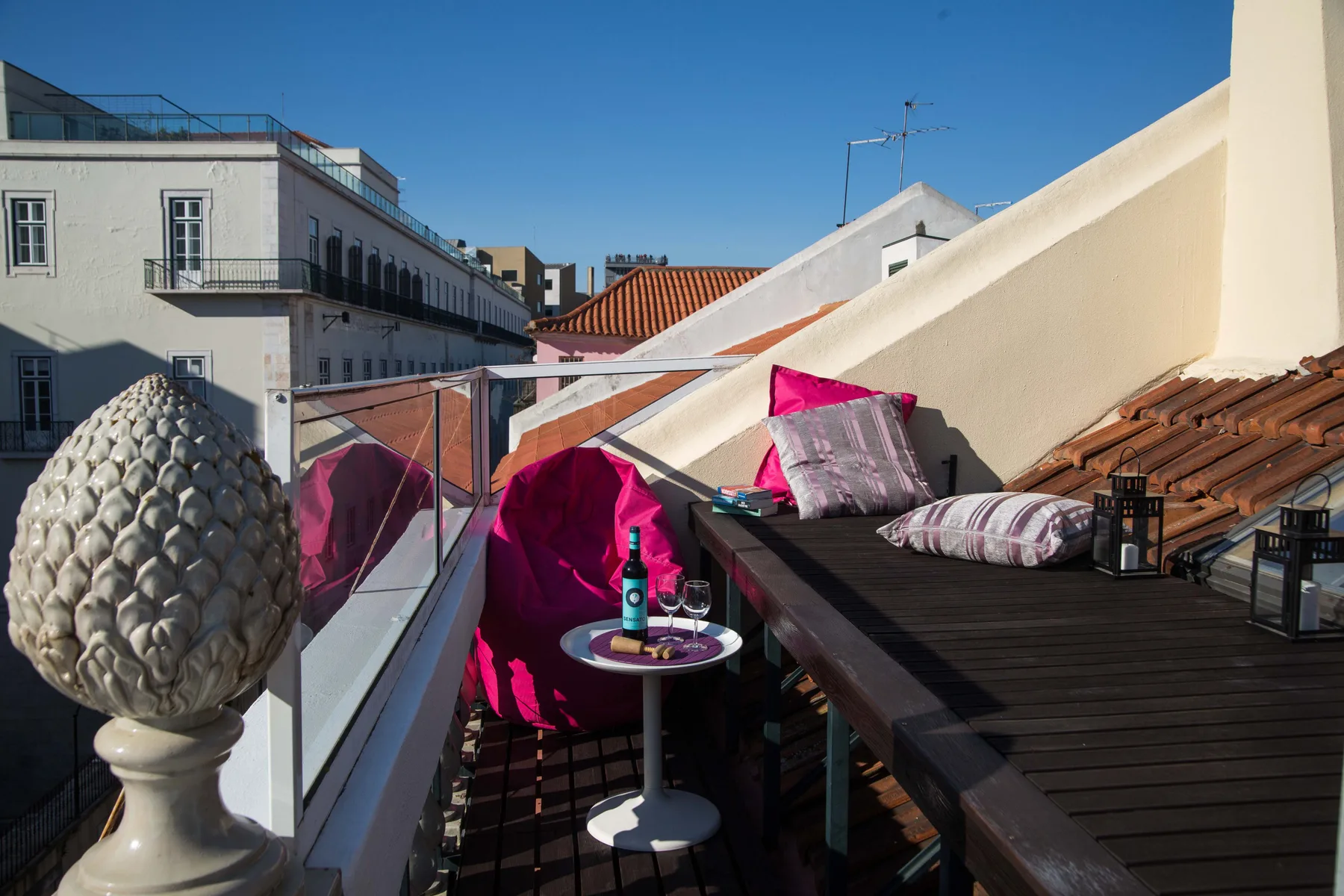 A rooftop terrace has seating beside a dark outdoor table and colorful cushions.