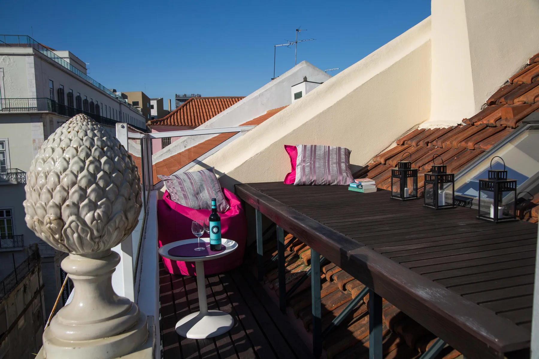 A rooftop terrace with a dark table, cushions, and views of nearby rooftops.