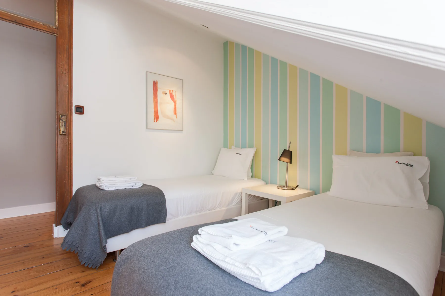 A bedroom with two beds, striped wall accents, and folded white linens.