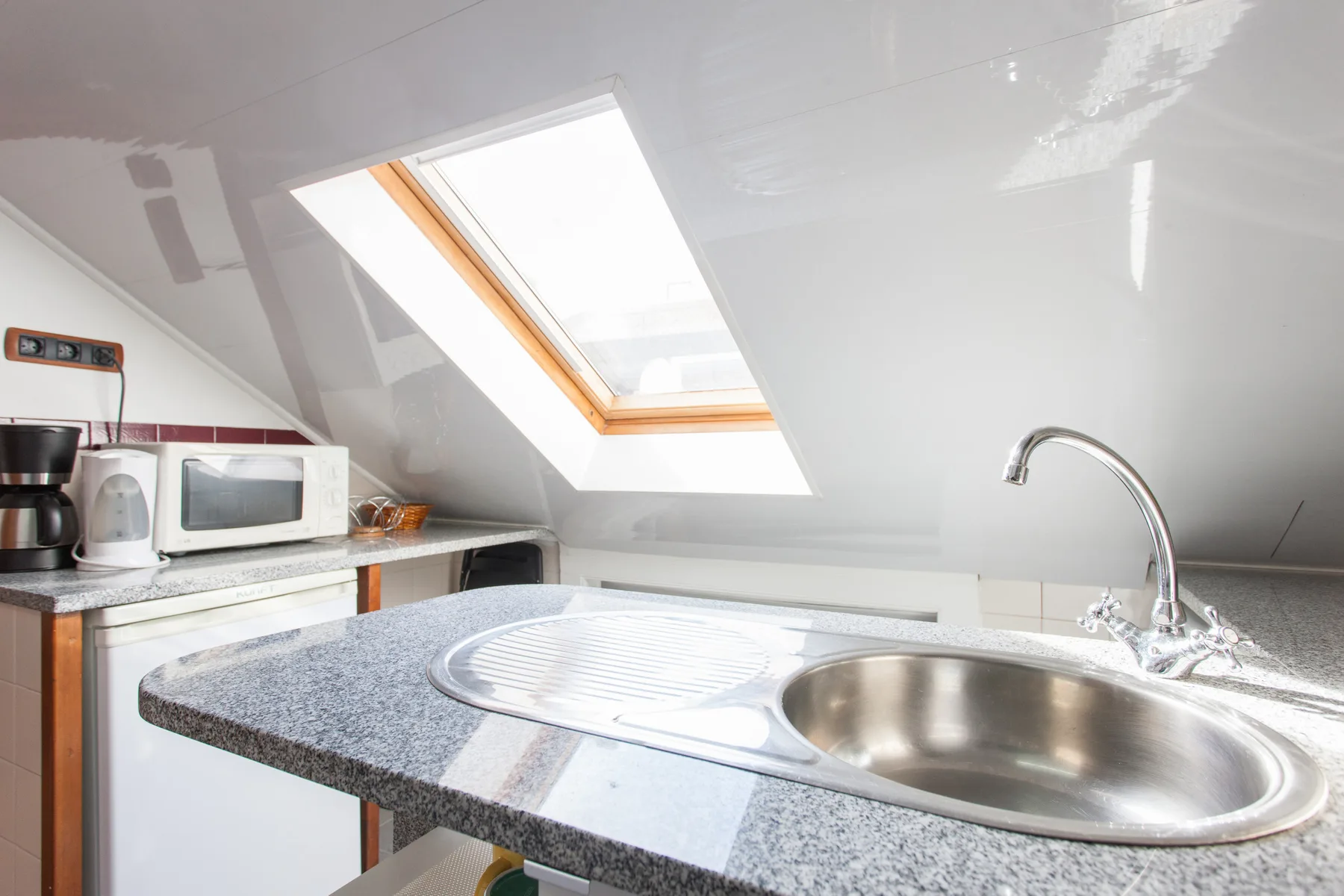 A compact kitchen with a countertop sink beneath a sloped ceiling and skylight.