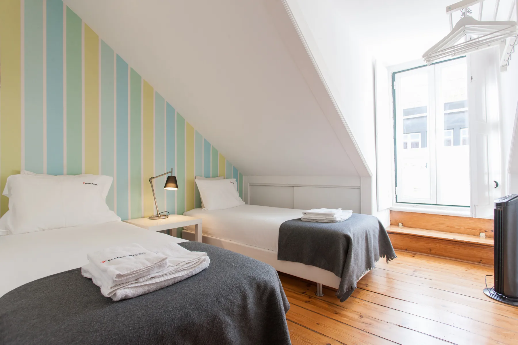 A bright bedroom with two beds, striped wall panels, and a large window.