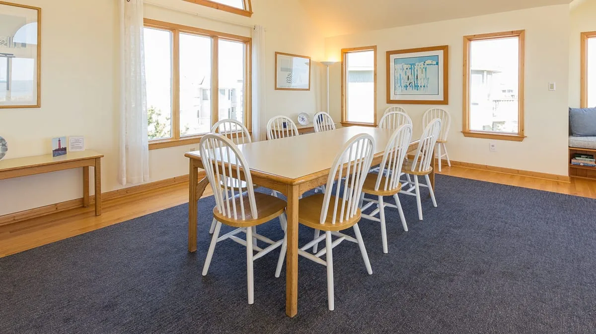 A dining area with a long table and chairs on a carpeted floor.