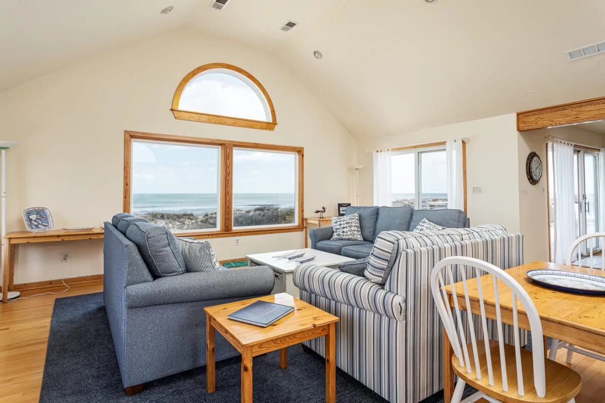A bright living room with seating, large windows, and a view of the water.