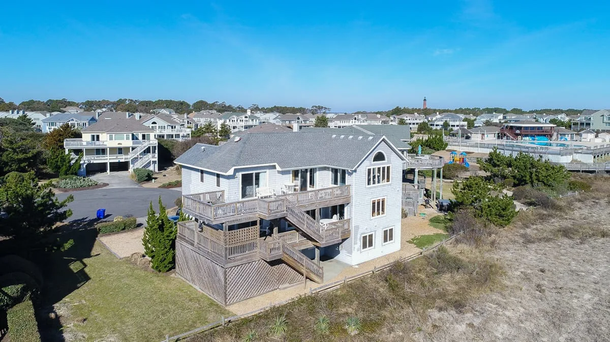 Aerial view of a coastal neighborhood with a large raised house in the foreground.