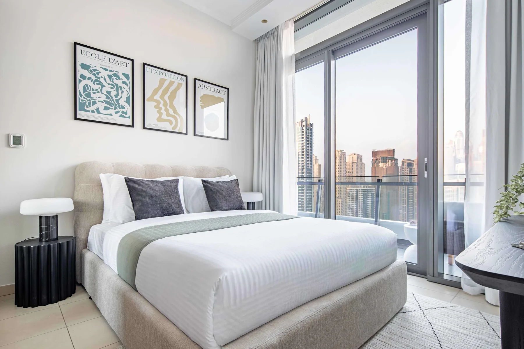 A bright bedroom with a neatly made bed beside floor-to-ceiling windows.