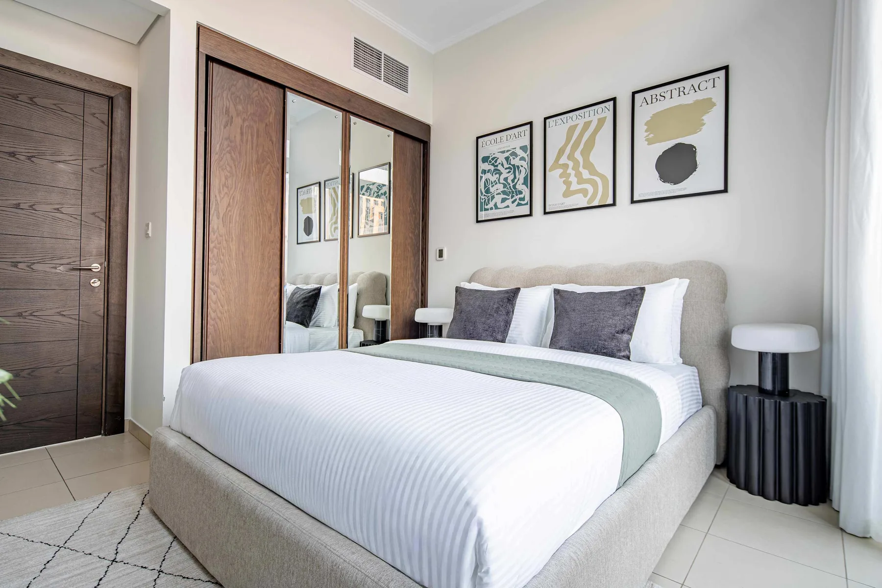 A bright bedroom with a neatly made bed and framed abstract prints.