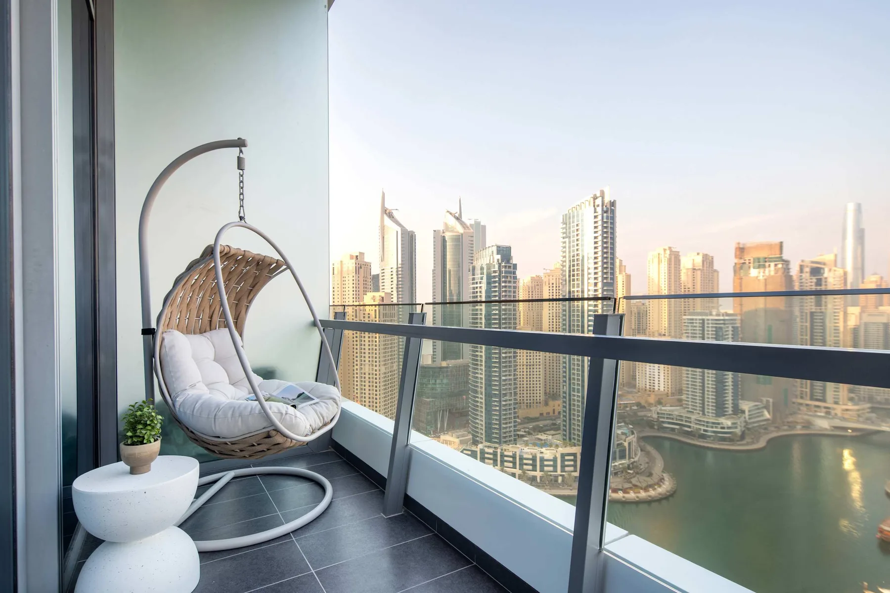 A balcony seating area overlooks a waterfront skyline through a glass railing.