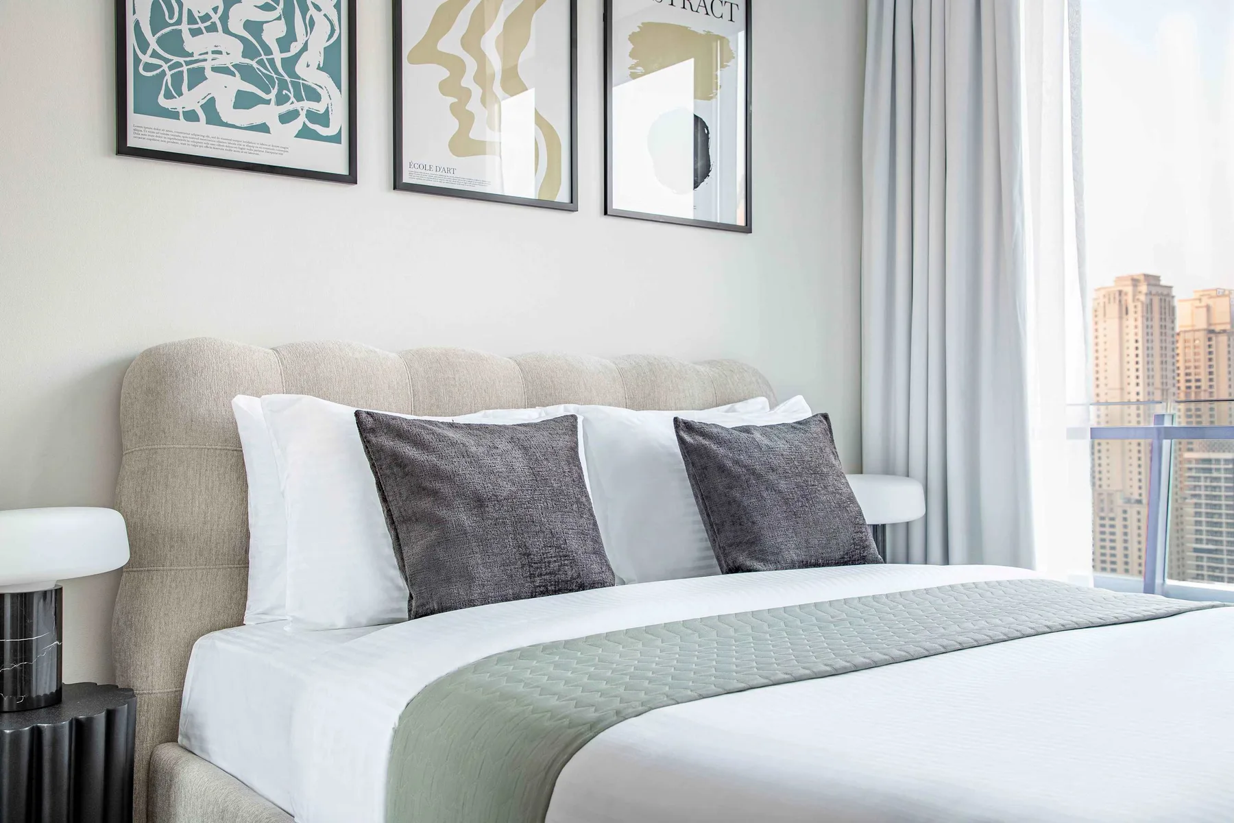 A neatly made bedroom with a padded headboard and framed artwork above the bed.