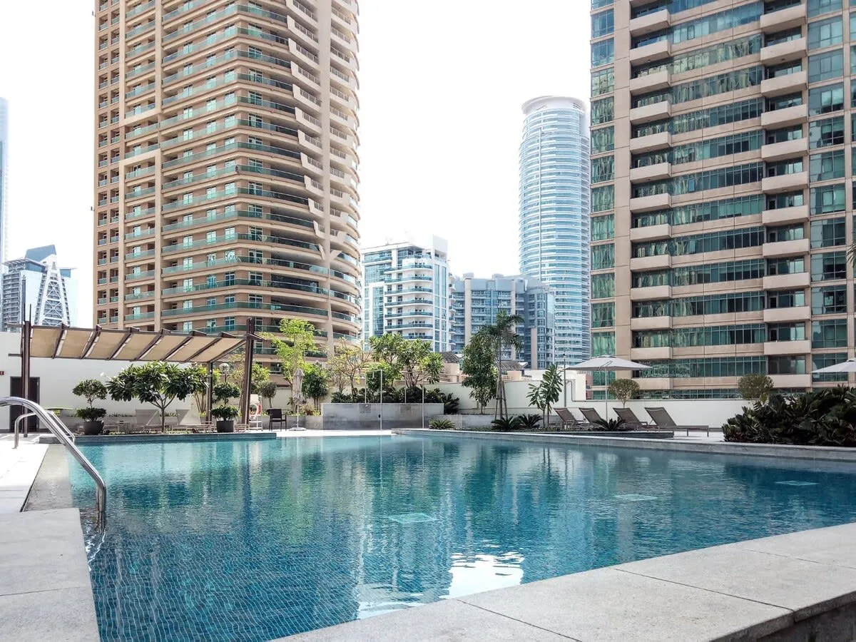 An outdoor swimming pool sits among tall apartment buildings.