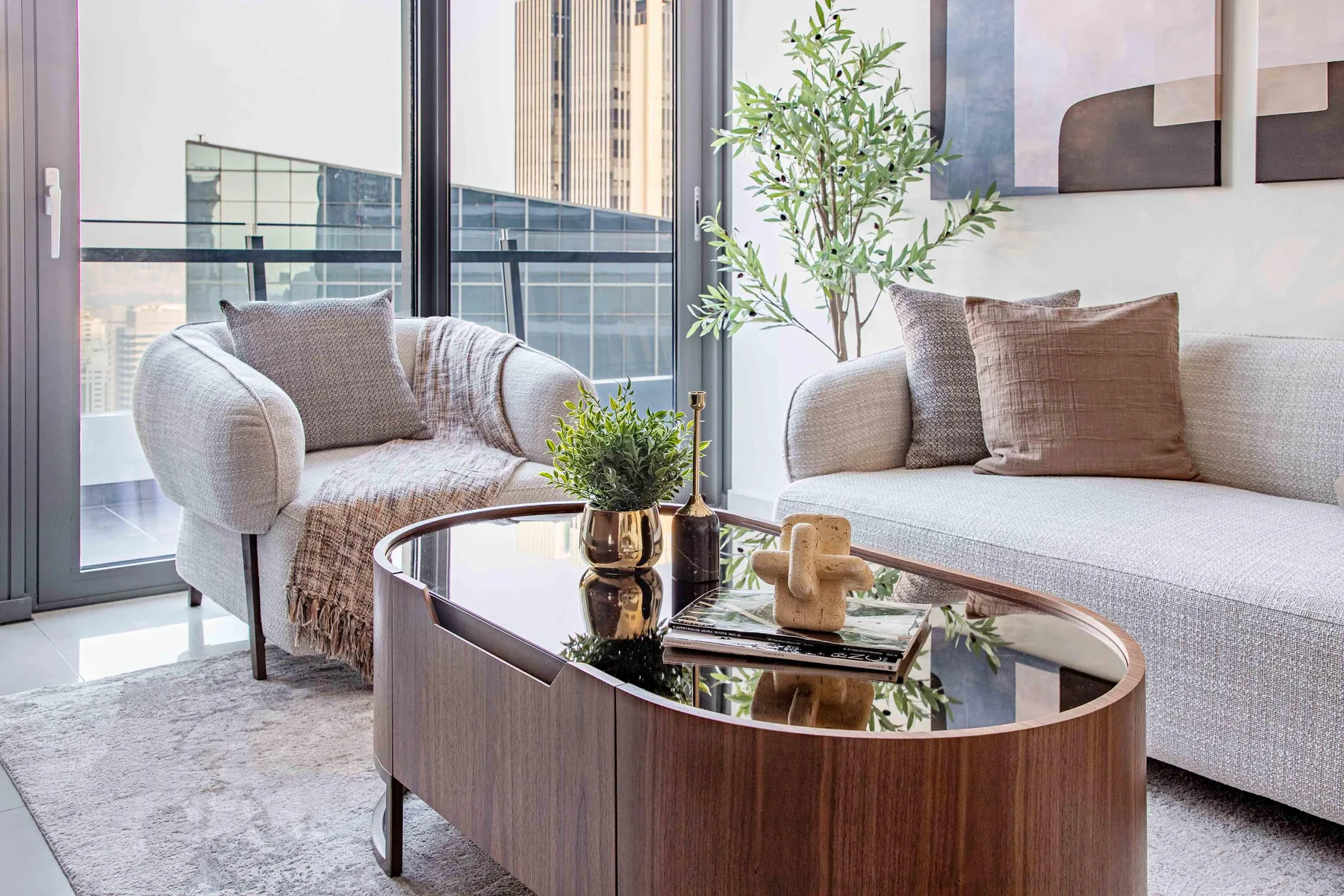 A bright living room with seating beside large windows and a glass-topped coffee table.