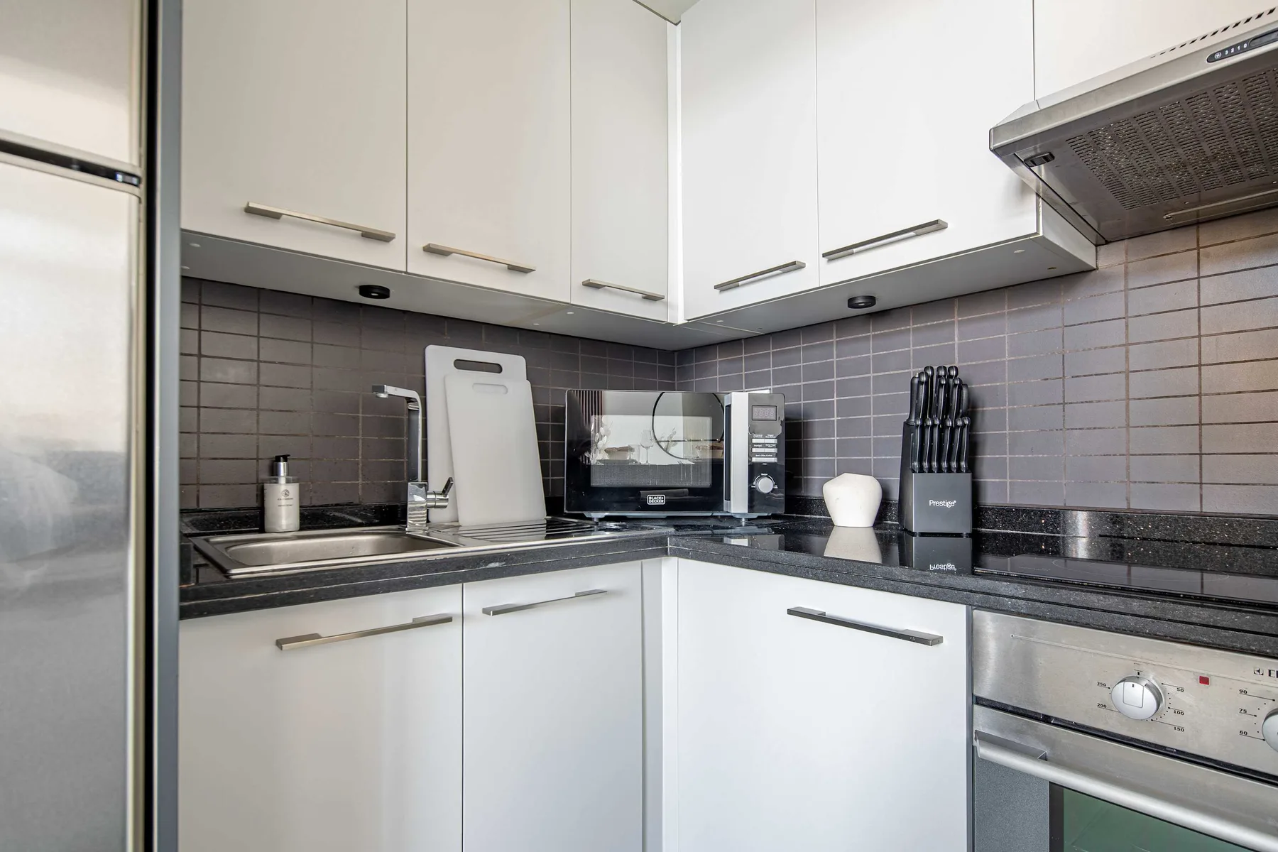 A modern kitchen with white cabinets, dark countertops, and stainless steel appliances.
