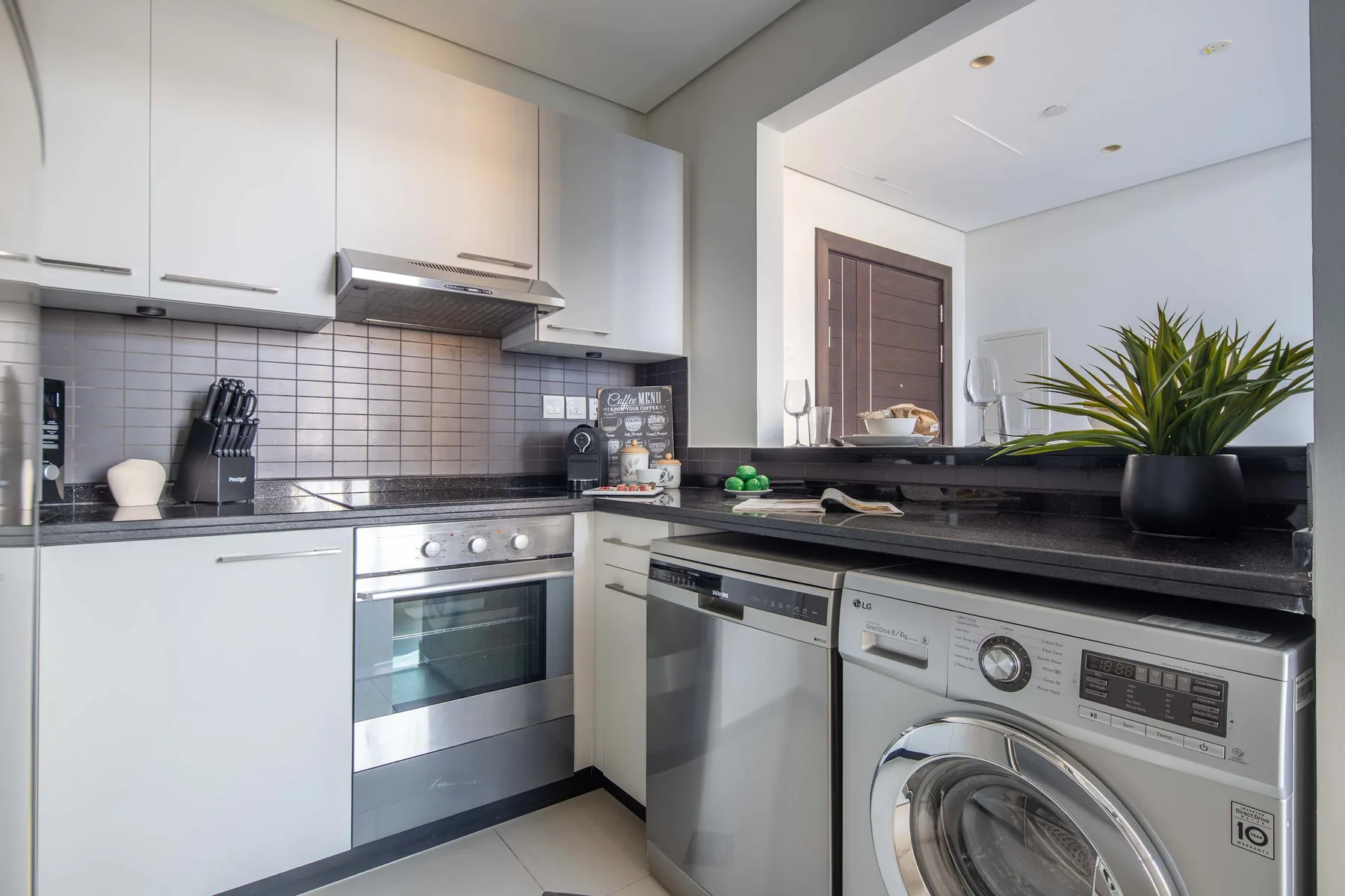 A modern kitchen with white cabinets, a cooktop, and stainless steel appliances.