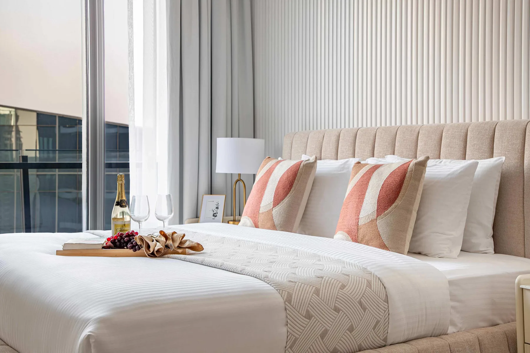 A neatly made bedroom with a bed, patterned pillows, and tall curtains.