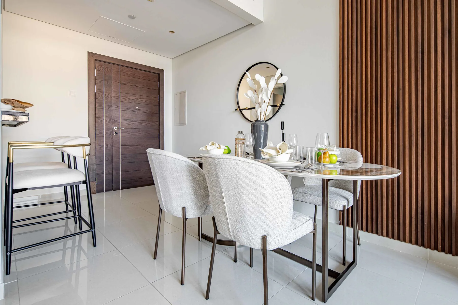 A dining area with a glass table and upholstered seating beside a wood-slat wall.