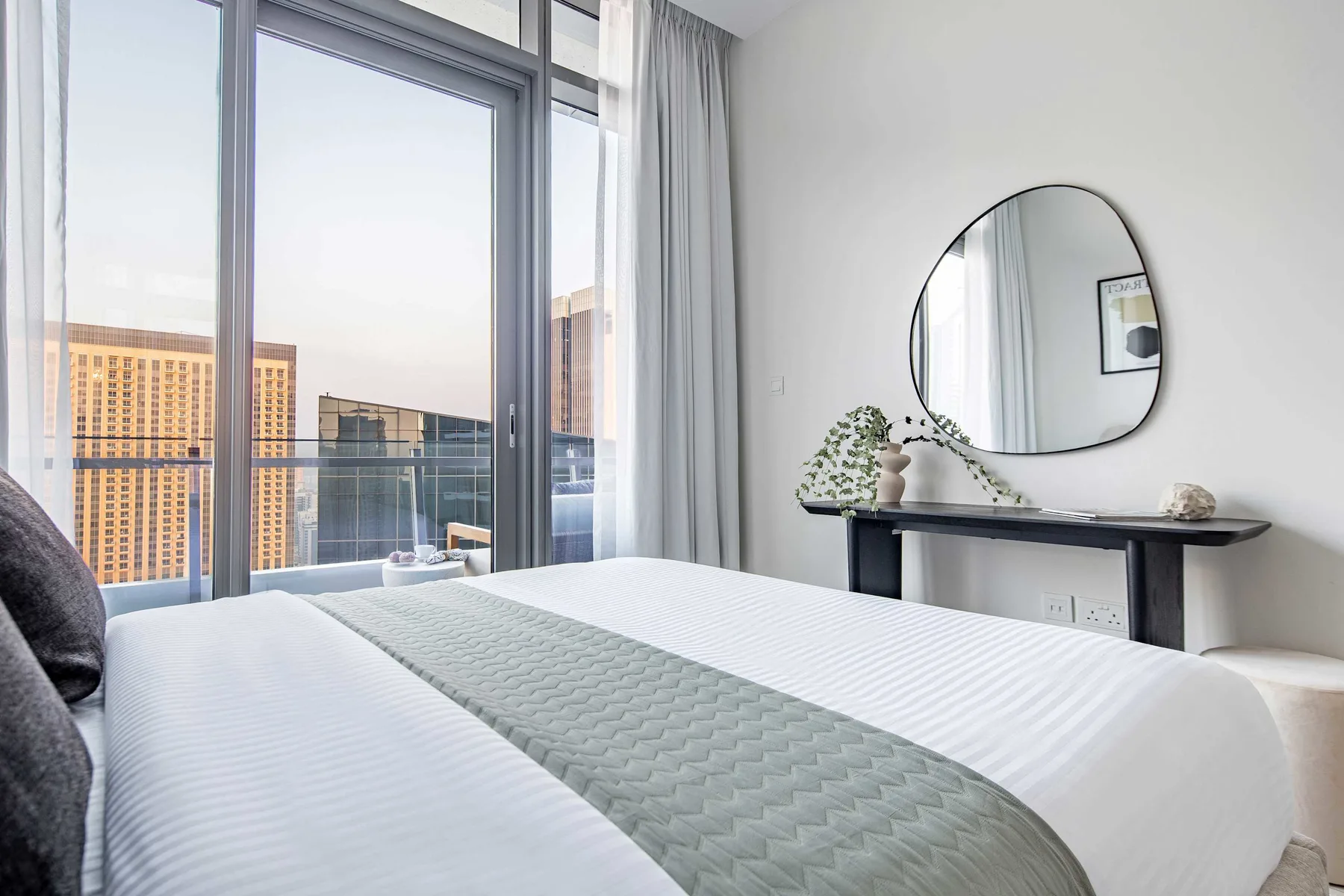 A bedroom with a neatly made bed beside floor-to-ceiling windows.