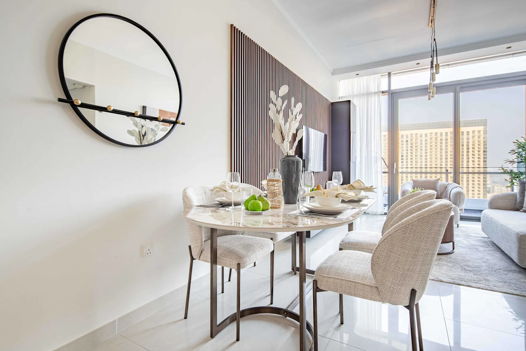 A bright dining area with a set table beside a living room and large windows.