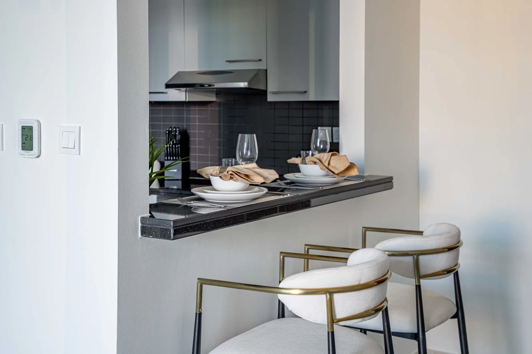 A modern kitchen counter opens to a small dining area with white seating.