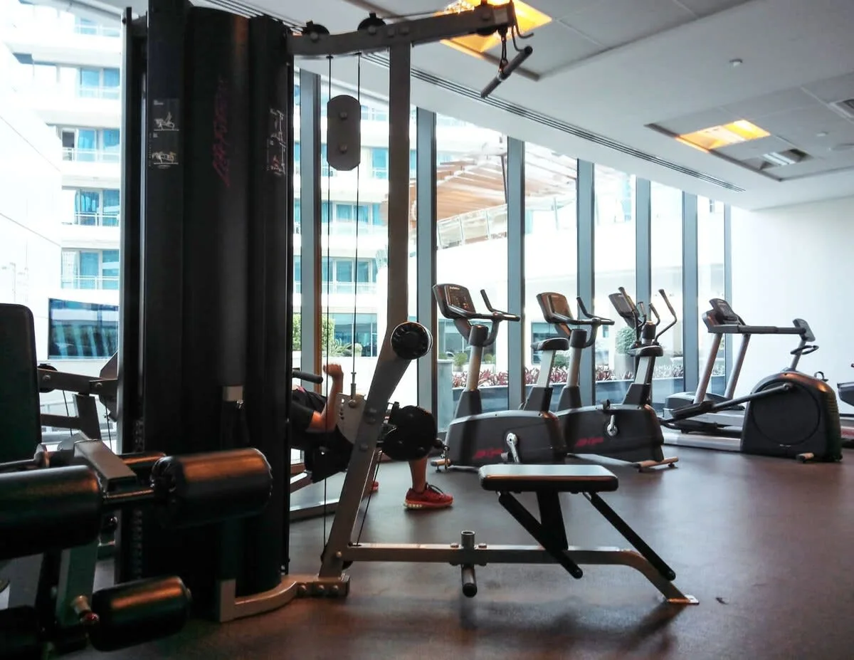 A gym with exercise machines and treadmills beside large windows.