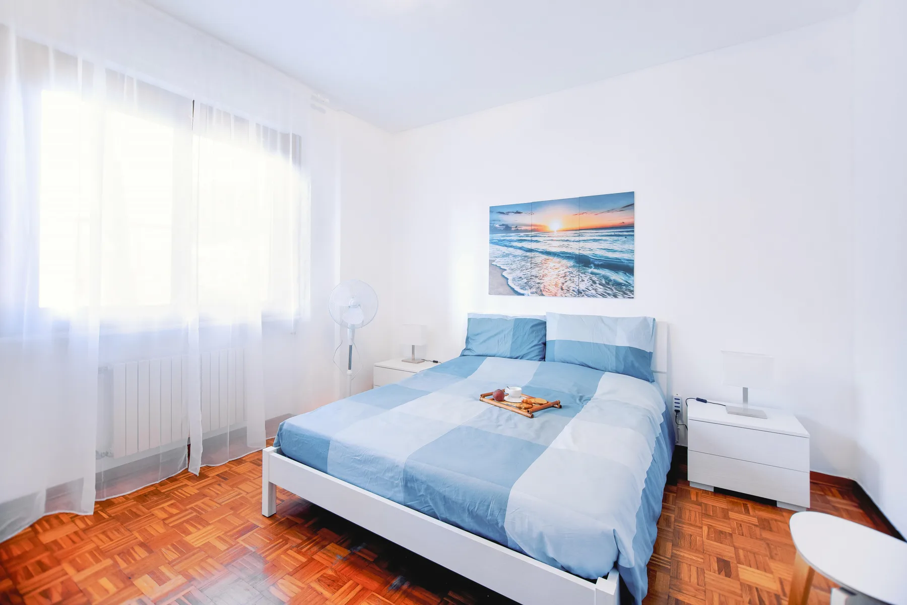 A bright bedroom with a bed beneath a beach photograph.