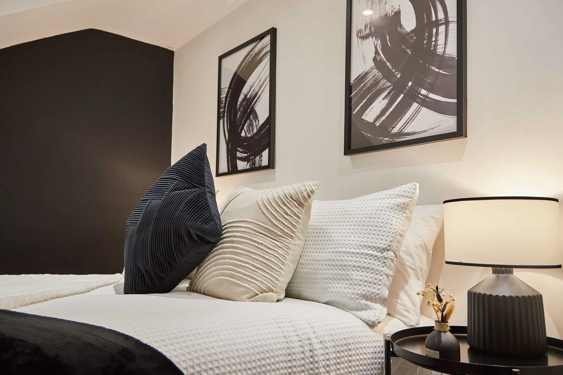 A bedroom with a bed dressed in light bedding and abstract wall art.