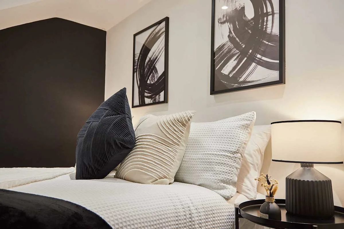 A bedroom with a neatly made bed and abstract artwork above it.