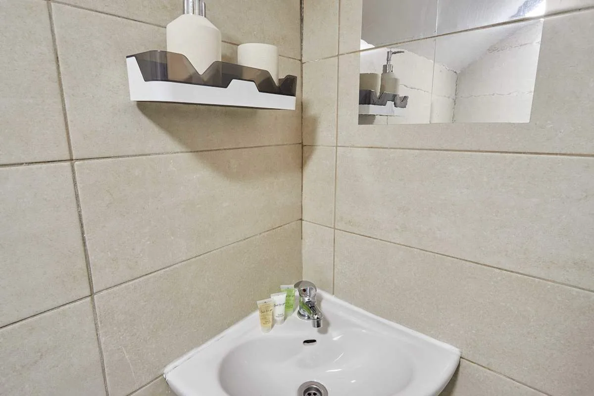 A bathroom sink beneath a small wall shelf and mirror.