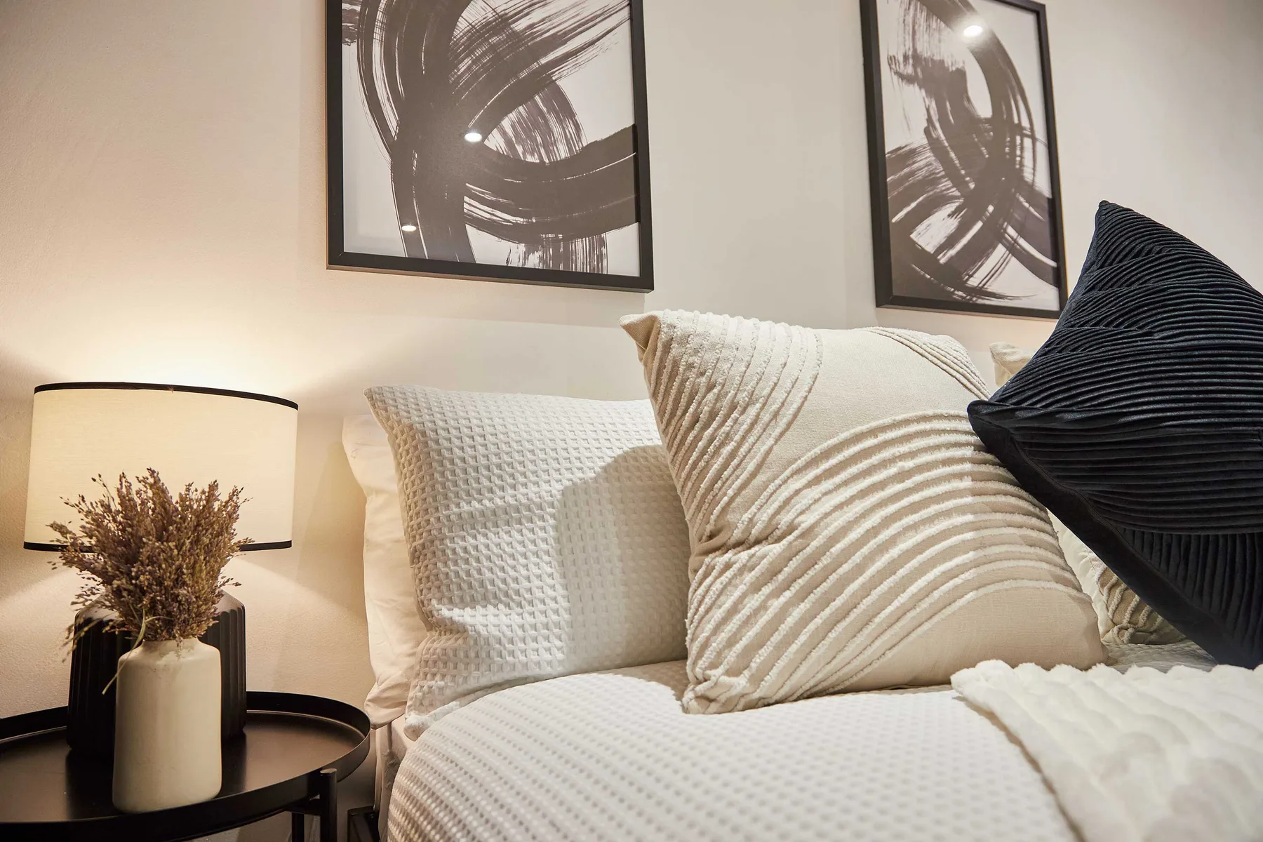 A bed with layered pillows sits beneath abstract wall art.