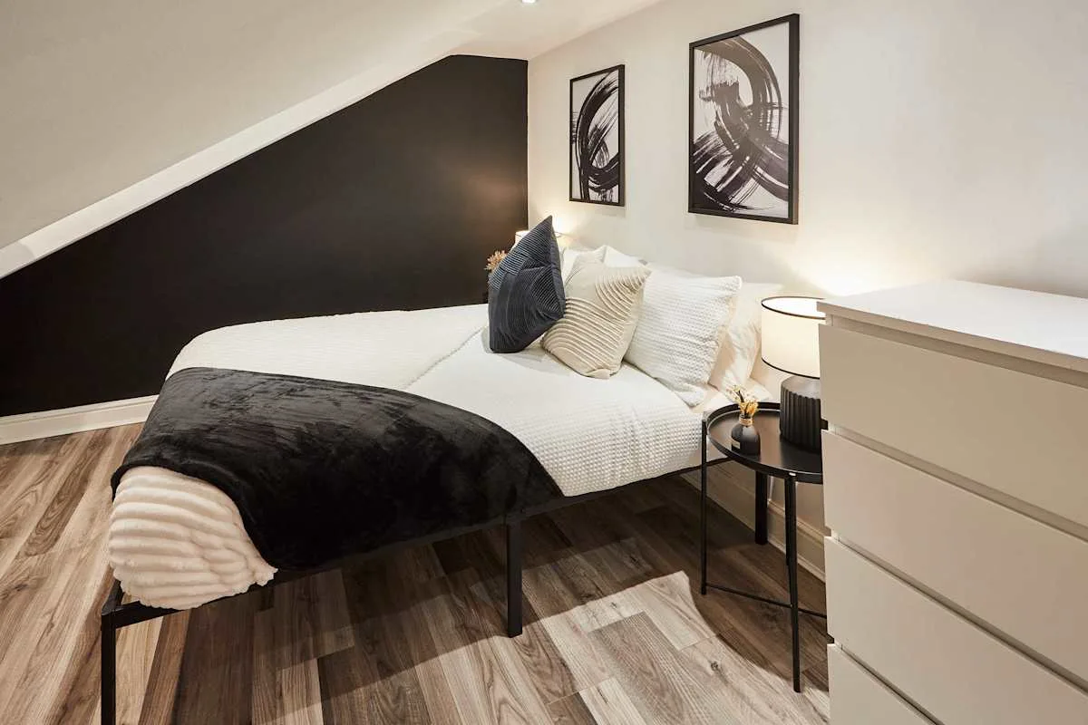 A bedroom with a bed dressed in white bedding and a dark throw.