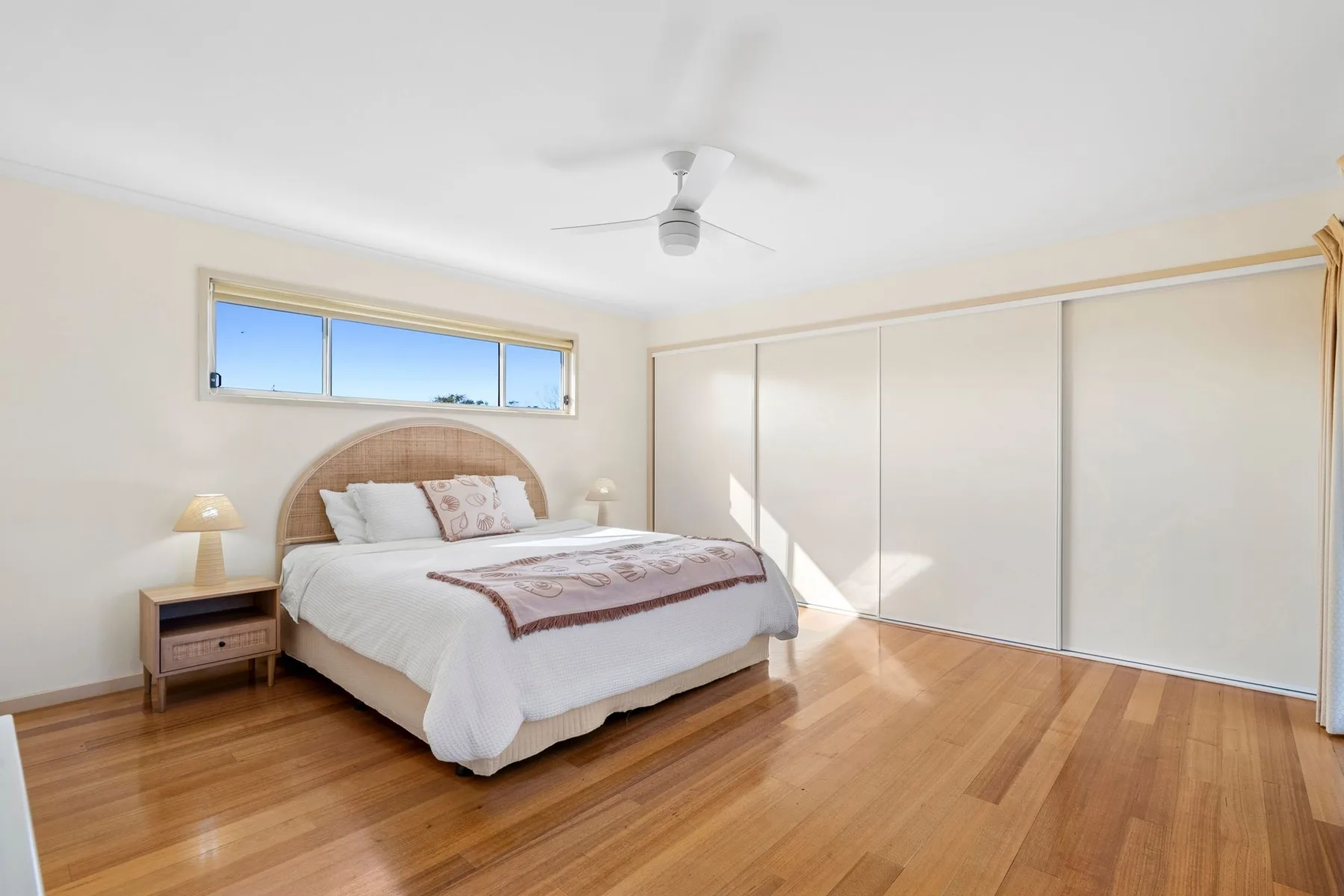 A bright bedroom with a bed, wood flooring, and wide built-in closets.