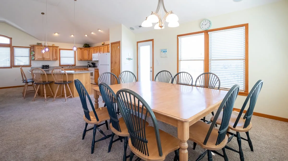 Un comedor con una gran mesa de madera y la cocina abierta al fondo.