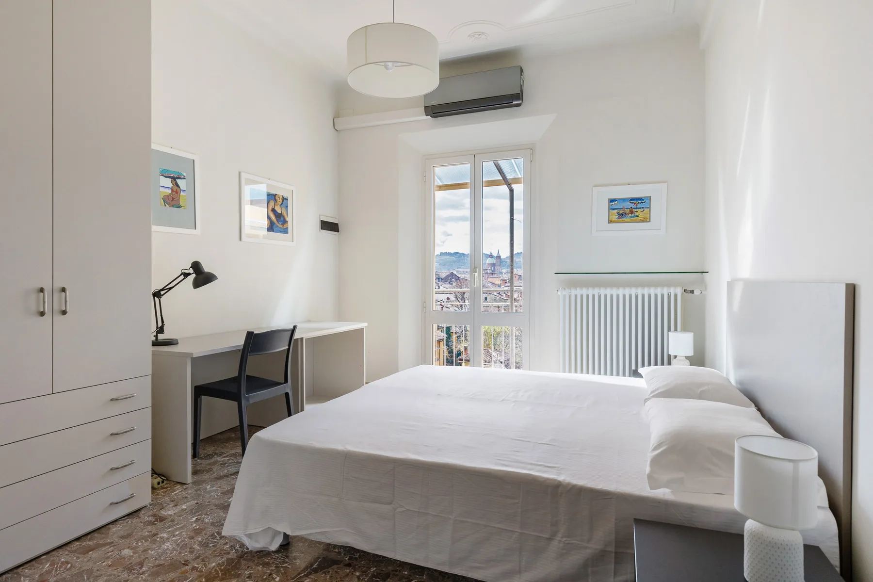 A bright bedroom with a neatly made bed, desk, and window.