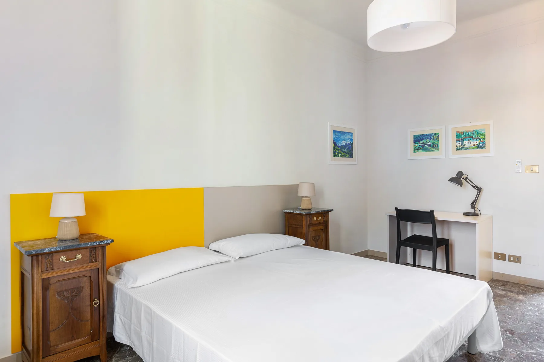 A bedroom with a double bed, yellow headboard, and desk against the wall.