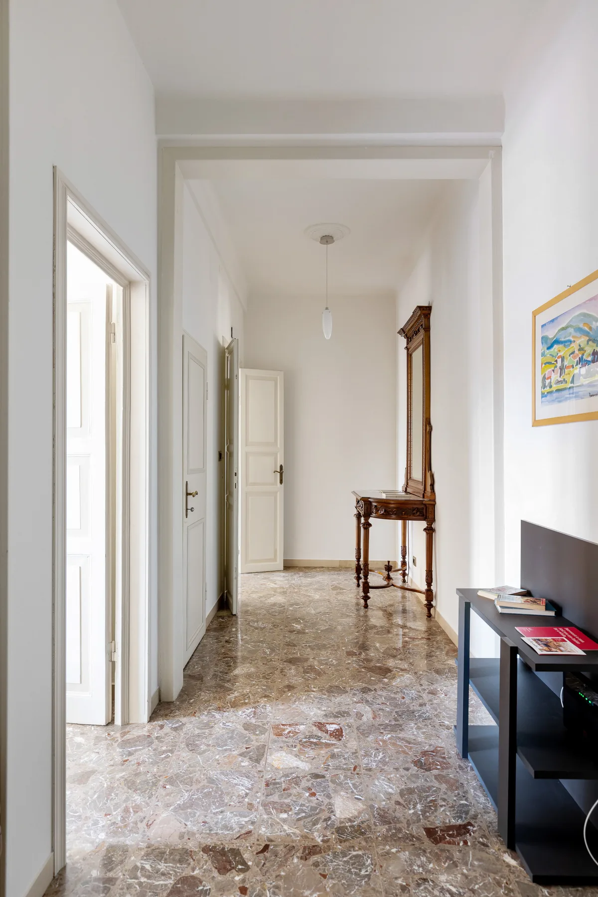 A bright hallway with a marble-patterned floor and a narrow console table.