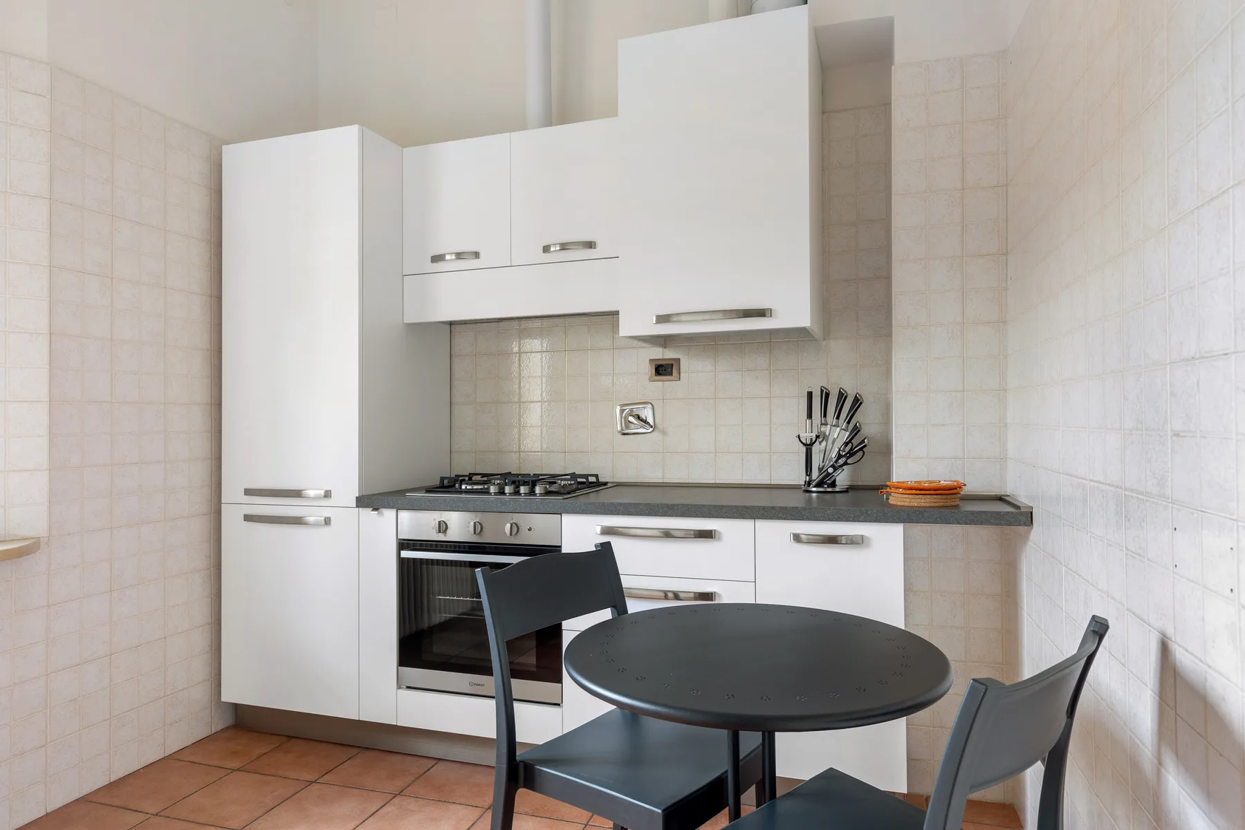 A compact kitchen with white cabinets, a cooktop, and a round dining table.