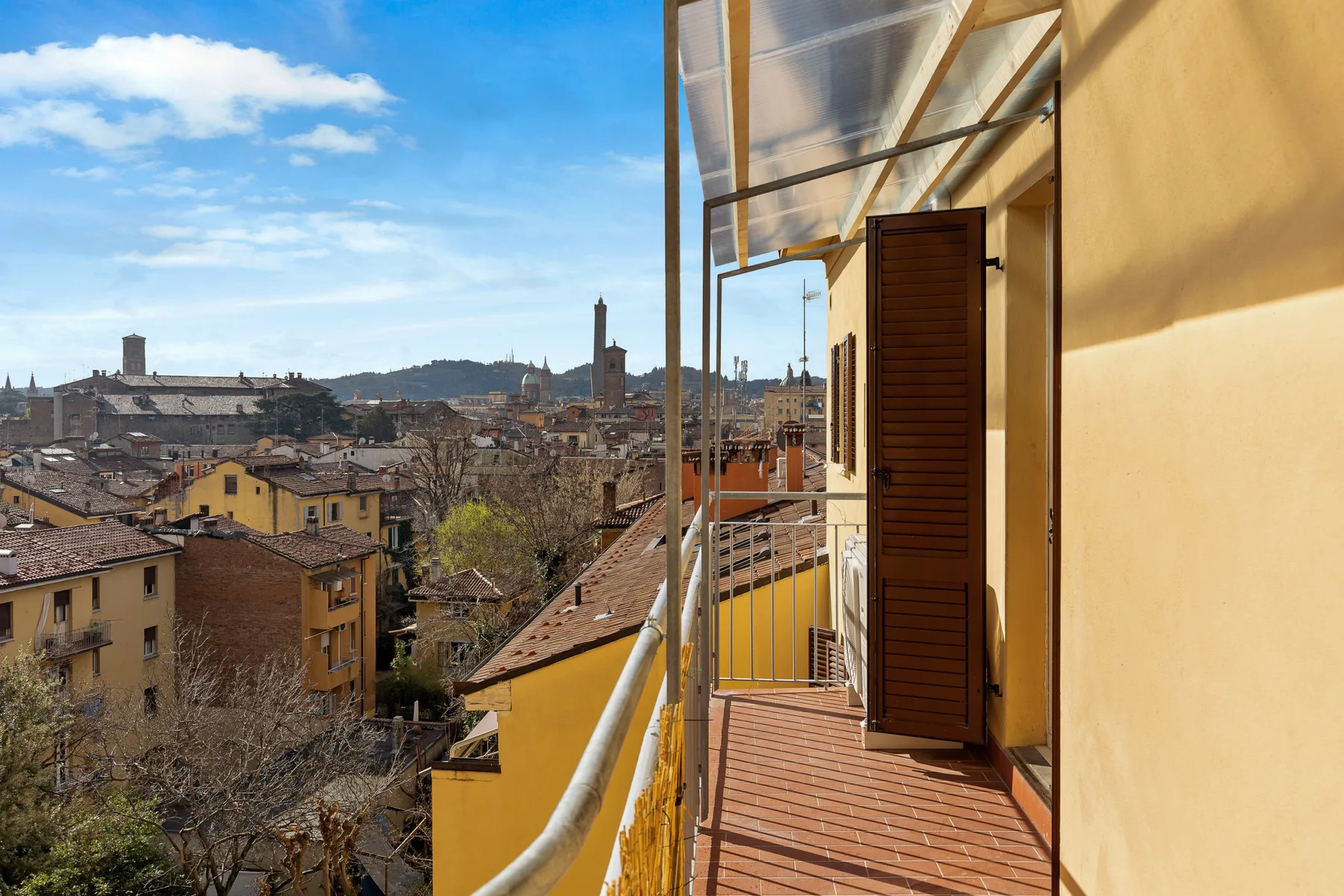 A narrow balcony overlooks a dense cityscape, with a wooden shutter open beside the doorway.