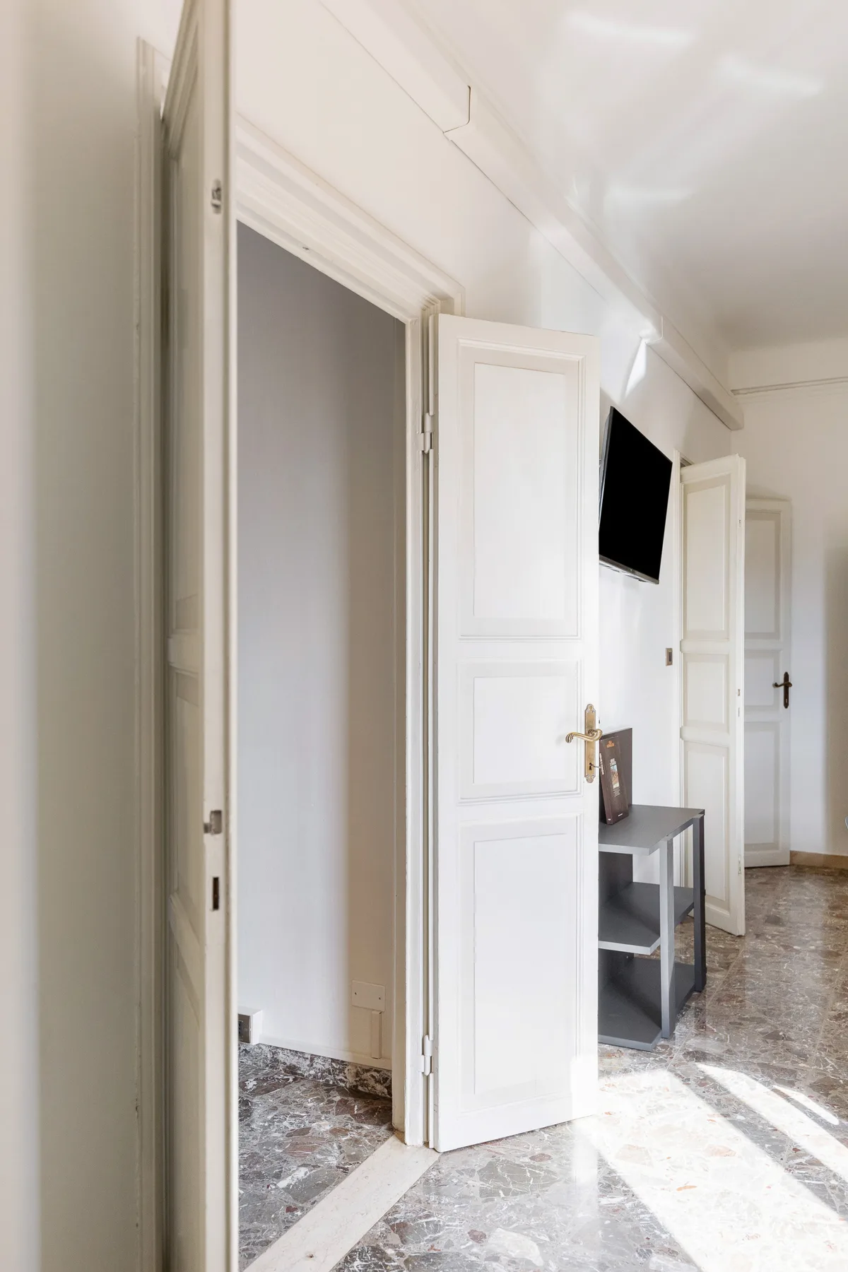 A bright interior hallway with open white doors and a wall-mounted television.