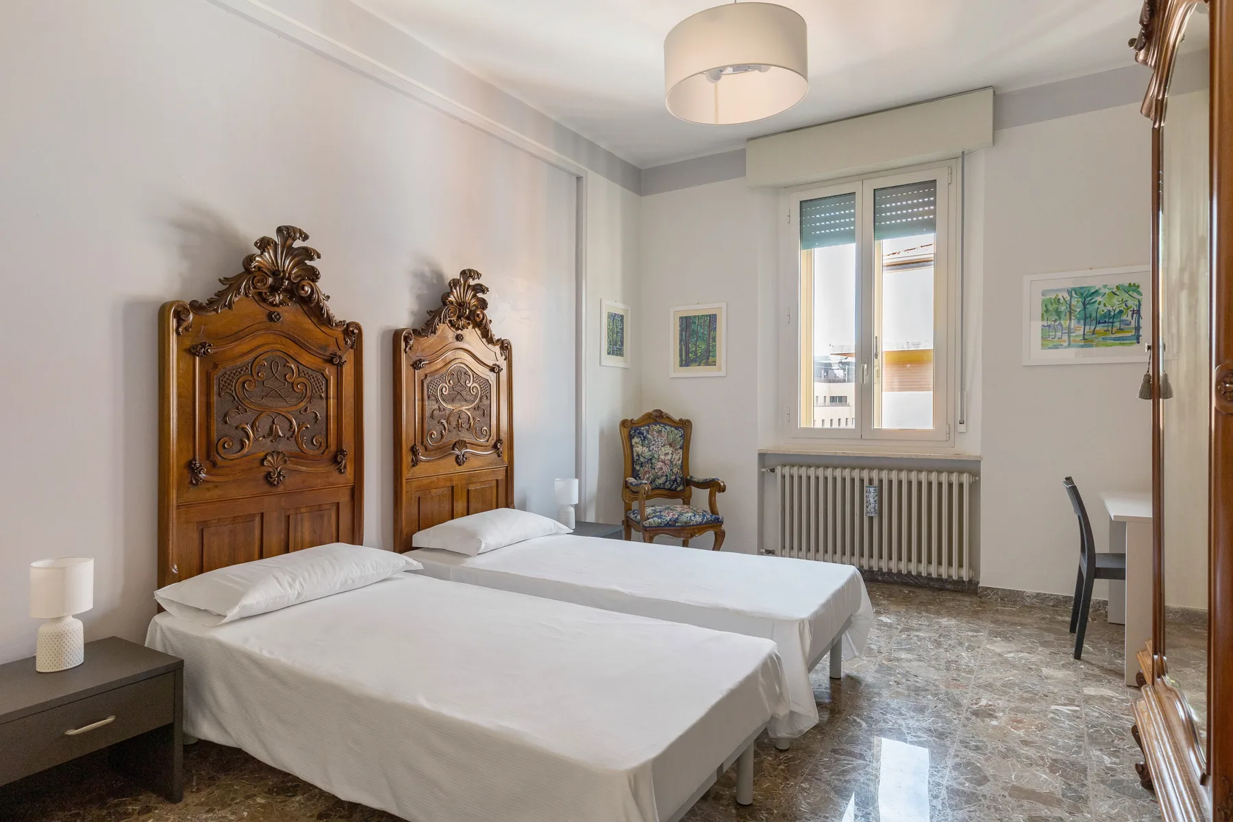 A bedroom with two beds, ornate wooden headboards, and a window overlooking the radiator.