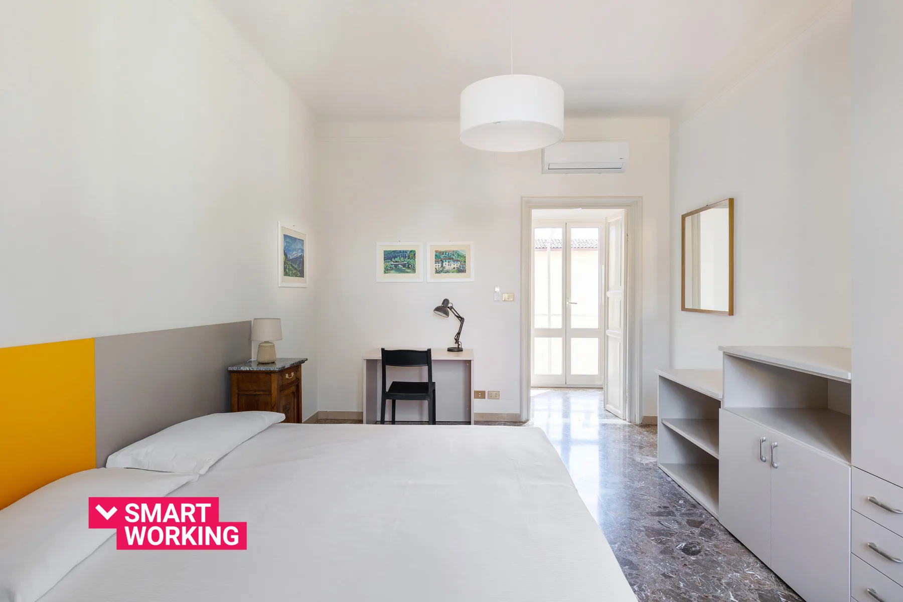 A bright bedroom with a bed, desk, and built-in shelving.