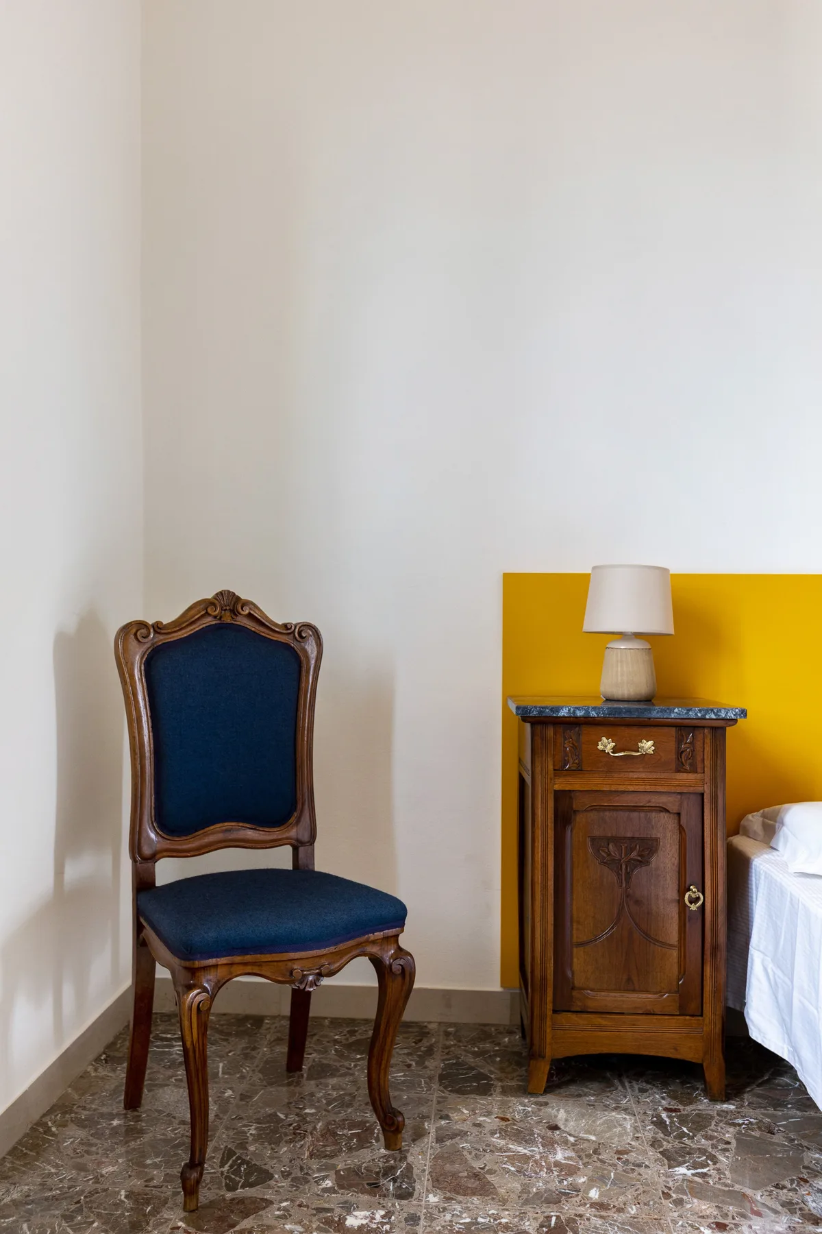 A bedroom with a wooden bedside table and an upholstered chair.