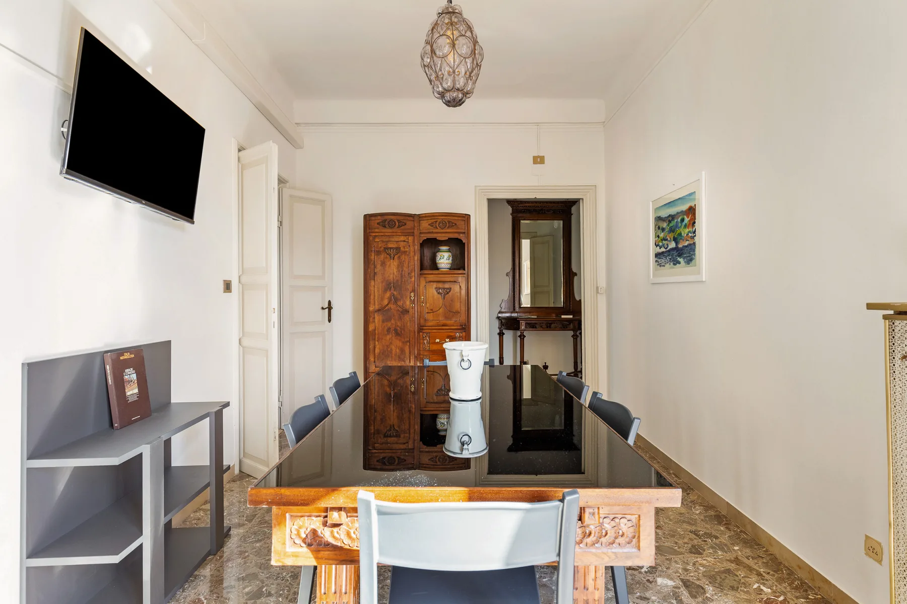 A dining room with a long table, chairs, and a wooden cabinet.