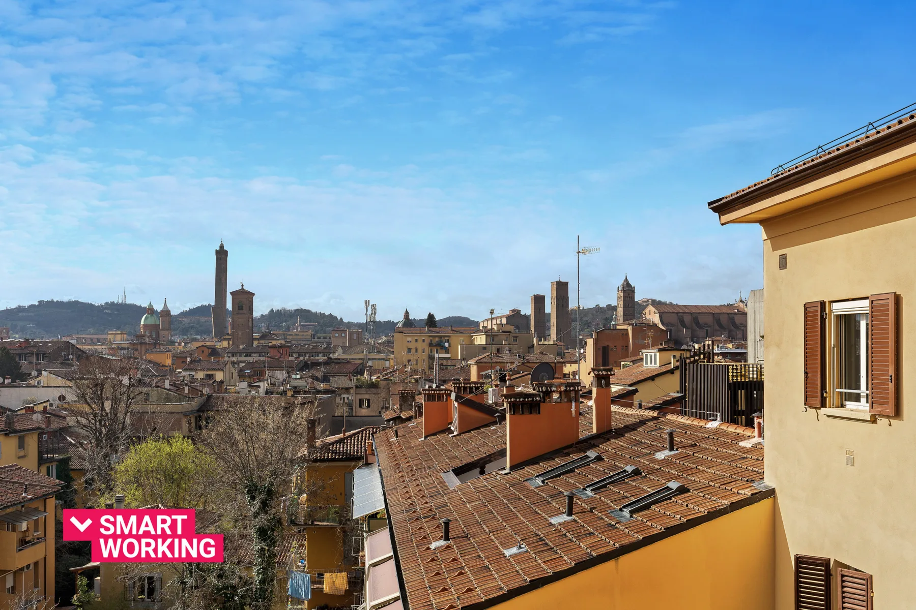 A city skyline with terracotta rooftops and a prominent tower beneath a blue sky.