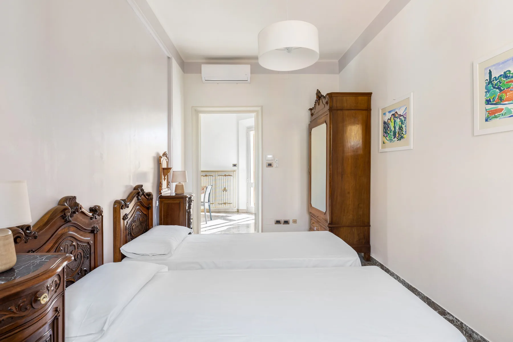 A bright bedroom with white bedding, carved wooden beds, and a tall wardrobe.