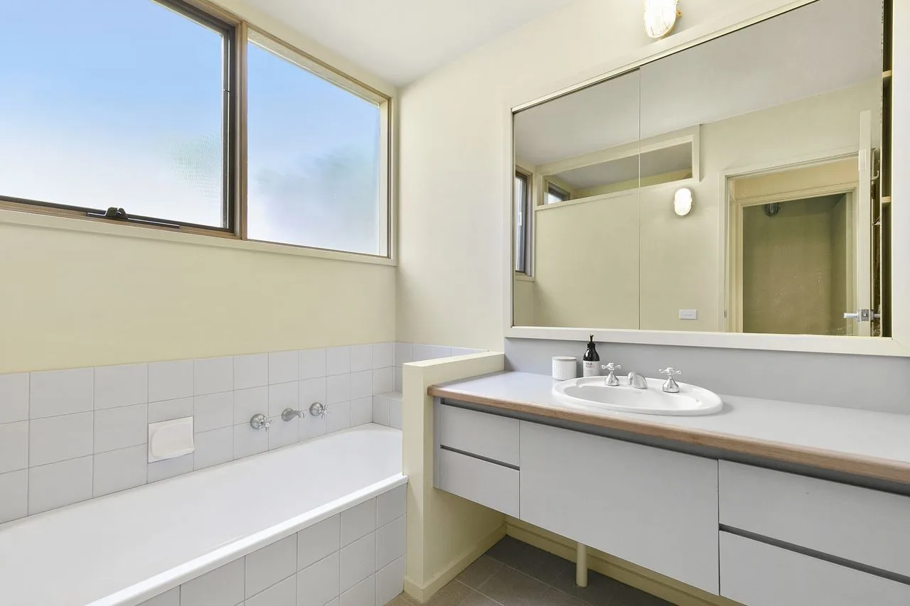 A bright bathroom with a bathtub, wide mirror, and sink.