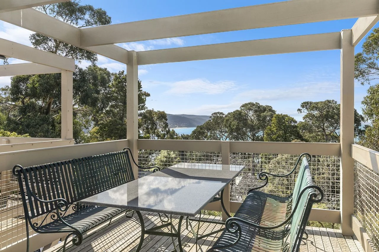 An outdoor patio has metal seating and a table overlooking trees and water.