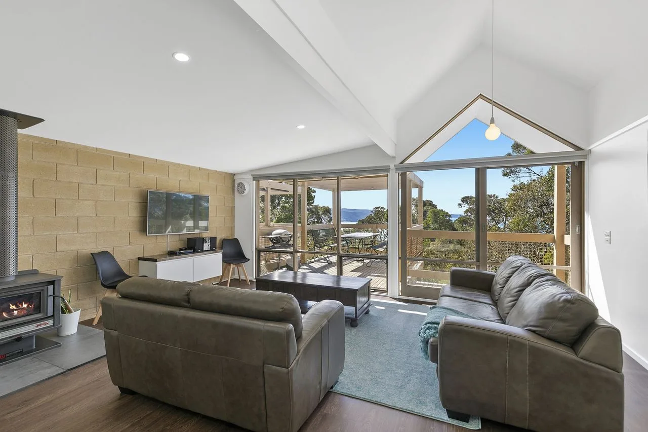 A bright living room with seating facing large windows and a view of trees.